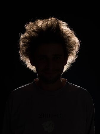 front view of man with tousled hair in black shadow on black backgroundの写真素材