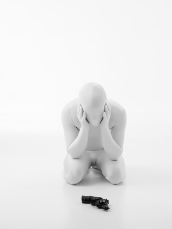 faceless man dressed in white, sitting on his knees, with gun in front of himの写真素材