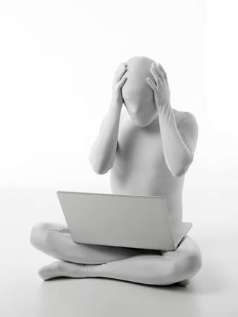 faceless man dressed white sitting with a laptop in lap hands on head worriedの写真素材
