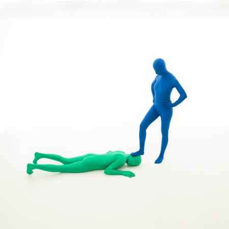 unknown woman dressed in blue sitting with her foot on the head of a green man with no face, lying downの写真素材