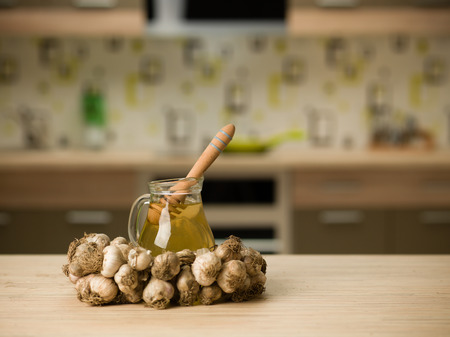 string of garlic surounding a jug with honey, on wooden kitchen tableの写真素材