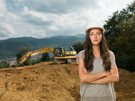 portrait of young caucasian female engineer on construction site with excavator in backgroundの写真素材