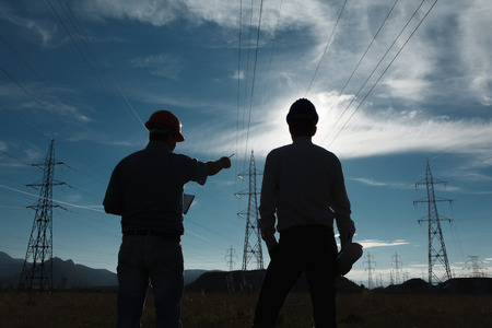 silhouette of two engineers standing at electricity station at sundownの写真素材