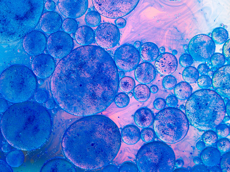 macro of oil drops and pigment on water surface with bright backgroundの写真素材