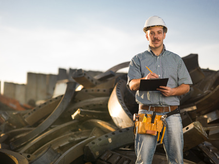 portrait of happy caucasian worker standing in metal landfill outdoors, writing