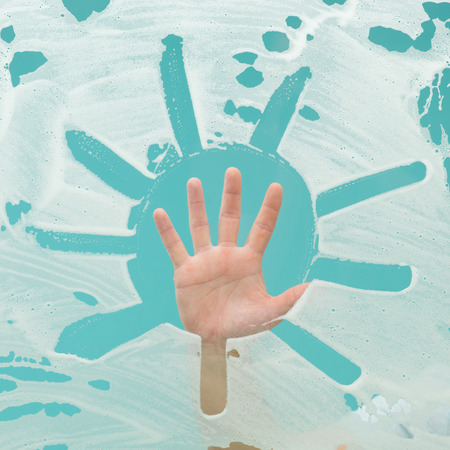 sun shape drawn with detergent on window surface and human hand  raised up in background