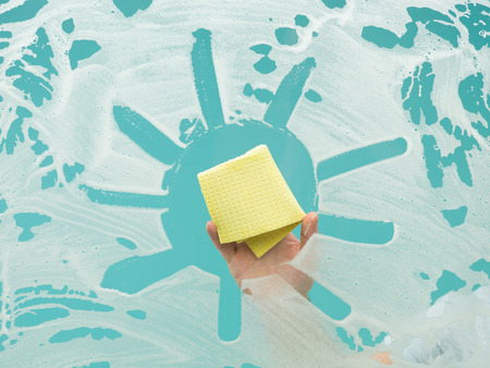 man cleaning window with detergent and drawing sun shape on it