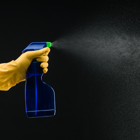 hand with rubber glove holding cleaning bottle and spraying liquid, on black backgroundの写真素材