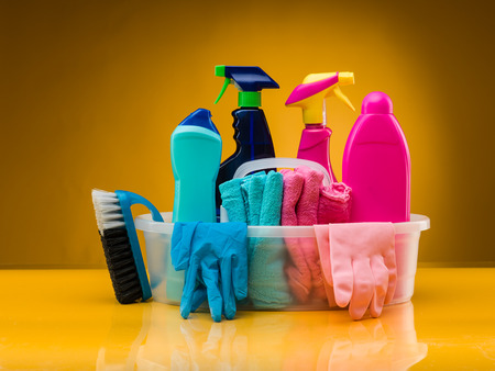 cleaning products and utensils in plastic basin against yellow backgroundの写真素材