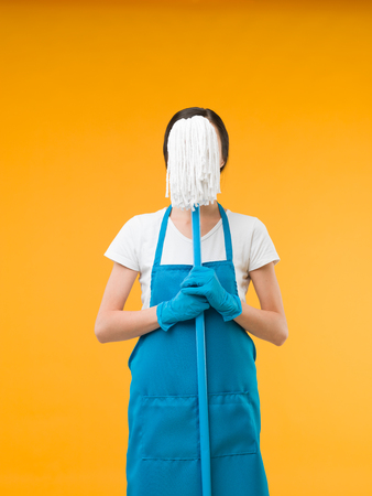 cleaning woman holding mop in front of her face, on yellow backgroundの写真素材