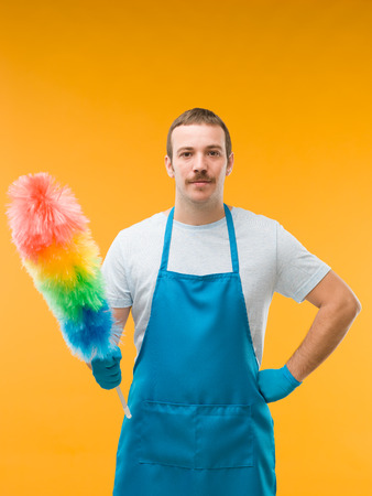 happy caucasian man standing and holding syntethic feather duster, on yellow backgroundの写真素材