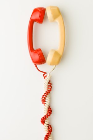 two handsets facing each other and talking, with cables tangled together. on white backgroundの写真素材