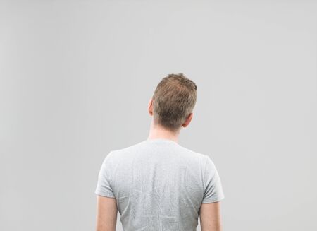rear view of man standing and looking away, against grey background. copy space available
