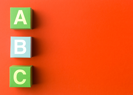 three colorful paper cubes with capital letters, in a row on red background. copy space availableの写真素材