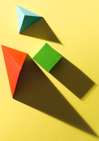 paper cube and pyramids with harsh shadow on yellow background