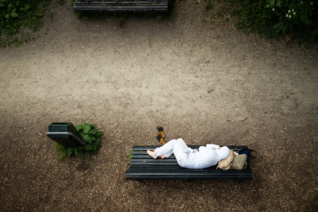 Homeless man dressed clean in white resting on a bench in the park 
luggage under headの写真素材
