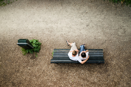 Caucasian young couple sitting on a park bench man protecting his girlfriend with loveの写真素材