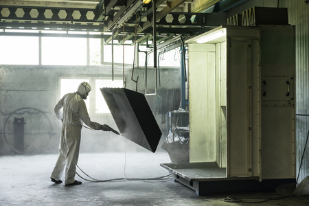 view of a worker wearing a full white protective suit and breathing mask, sand blasting a metal crate hung from a metal beam in the ceiling of an industrial hall view of a worker wearing a full white protective suit and breathing mask, sand blasting a metal crate hung from a metal beam in the ceiling of an industrial hall