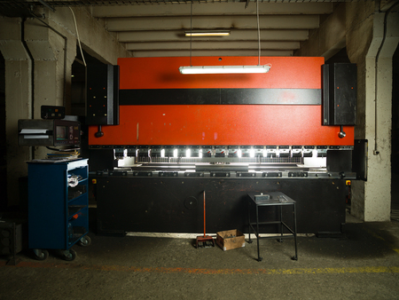 front view of an industrial machinery, painted in red and black, with a control panel and a table...