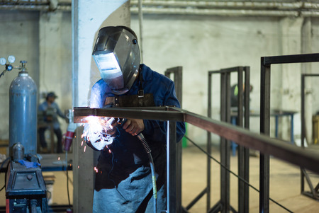 front close-up of a worker wearing protective gear, with mask and a leather apron, welding together...