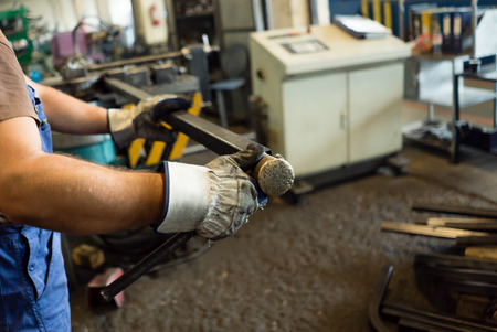 close-up of a man's hands in white heavy-duty gloves, holding and examining a square pipe, in an...