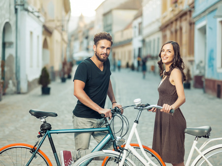 handsome man and beautiful woman met with bicycles in the old town , smiling for the cameraの写真素材