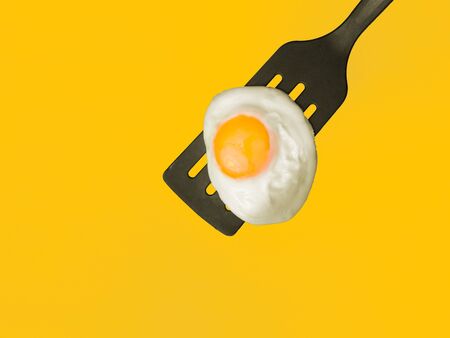 Sunny side up egg on a spatula 3/4-overhead view on yellow backgroundの写真素材