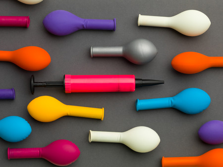pink balloon pump between  colourful deflated balloons,  on a grey background
