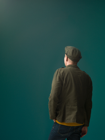 fashionable military style dressed person rear view looking at a dark aquamarine backgroundの写真素材