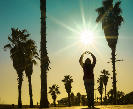A young girl making heart symbol with her hands at sunseの写真素材