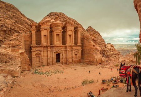 Petra, Jordan - January 13 2020: Tourists look tiny in front of the vast Monastery (El Deir), the largest monument on the archaeological site, built by the Nabataeans, on a cloudy day.のeditorial素材