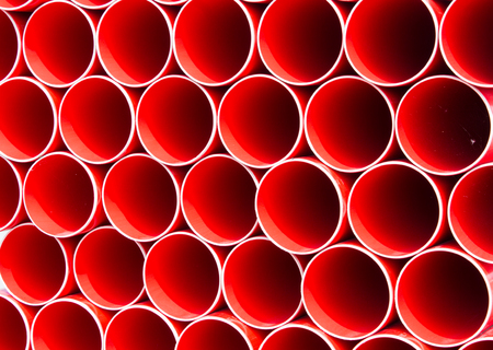 Stack of Red Construction pipes, the symmetry of evenly spaced pipework except for one pipe standing...