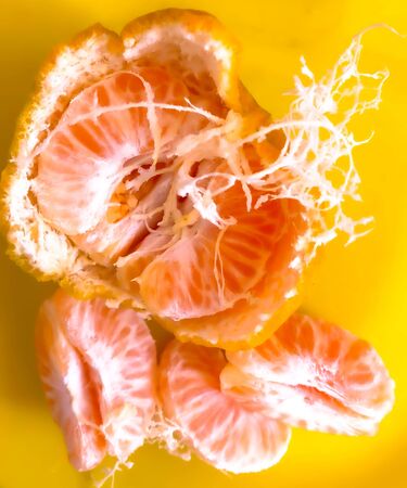 closeup fresh half peeled orange inside skin and pieces in the yellow backgroundの写真素材