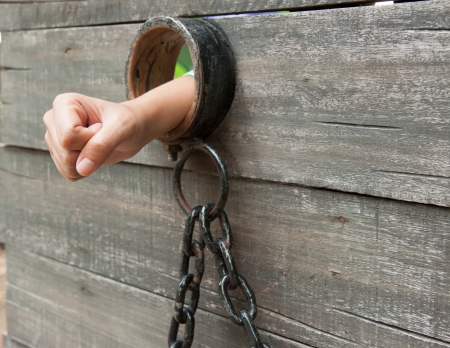 Locked Up hand is shackled to a vintage prison cell door with a ball and chainの写真素材