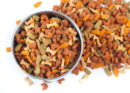 Silver bowl full and overflowing with dog food bits on a white backgroundの写真素材