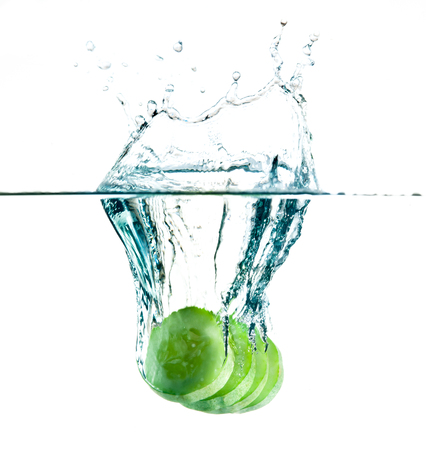 sliced cucumbers splashing water isolated on whiteの写真素材
