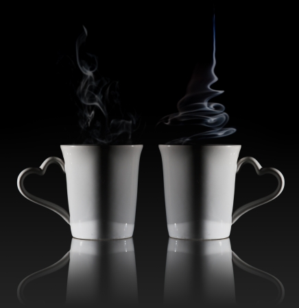 White cup of coffee with a dense smoke in the air, against a black background.の写真素材