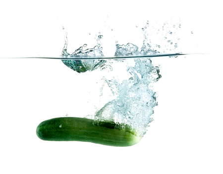 green cucumbers dropped into water isolated on whiteの写真素材