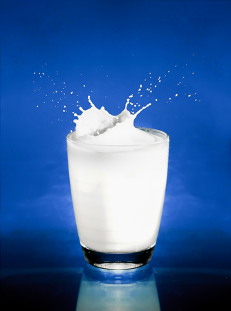 Splash of milk from the glass on a blue backgroundの写真素材