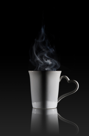 White cup of coffee with a dense smoke in the air, against a black background.の写真素材