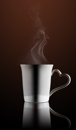 White cup of coffee with a dense smoke in the air, against a black background.の写真素材