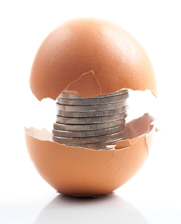 Coins in broken golden eggshell over white background.