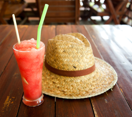 Glass of watermelon smoothie and a hat on a wooden tableの写真素材