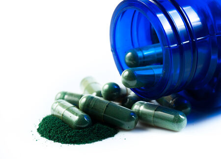 Green herb capsules spilling out of a bottleの写真素材