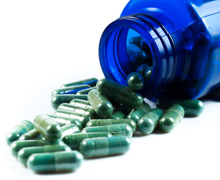 Green herb capsules spilling out of a bottleの写真素材
