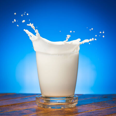 Splash of milk from the glass on a blue backgroundの写真素材