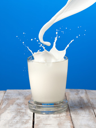 Splash of milk from the glass on a blue backgroundの写真素材