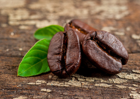Coffee grains and green leaf on grunge wooden backgroundの写真素材