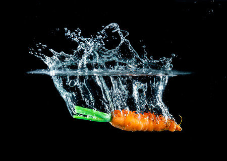 Carrot in the water splash over black background.の写真素材