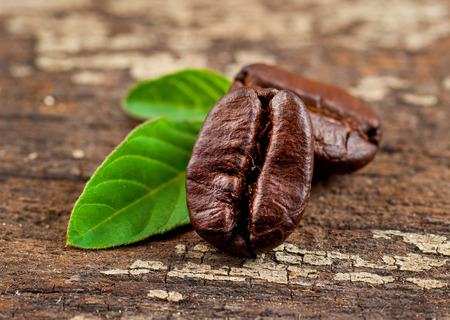 Coffee grains and green leaf on grunge wooden backgroundの写真素材
